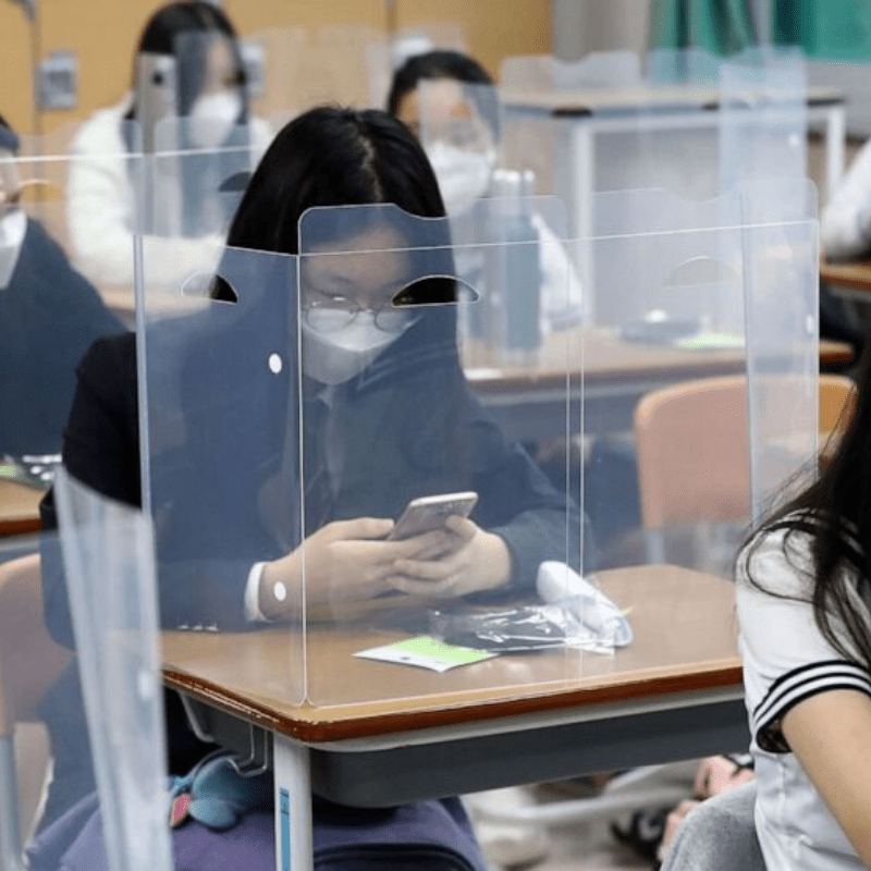 Korean students in the classroom with plastic shields around desks to protect against covid transmission